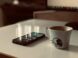 a cup of coffee next to a cell phone on a table