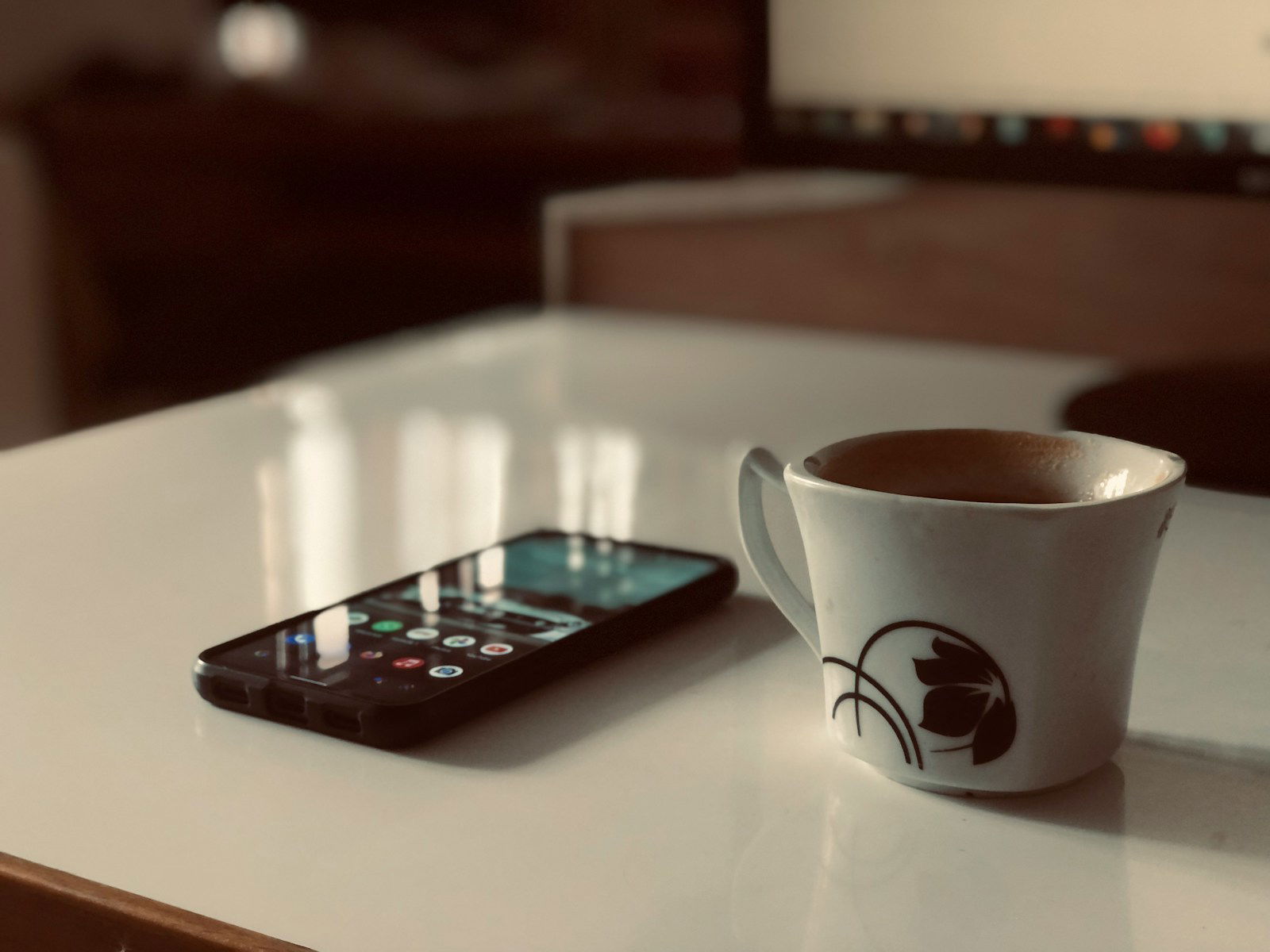 a cup of coffee next to a cell phone on a table