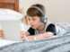 boy in blue shirt wearing headphones lying on bed