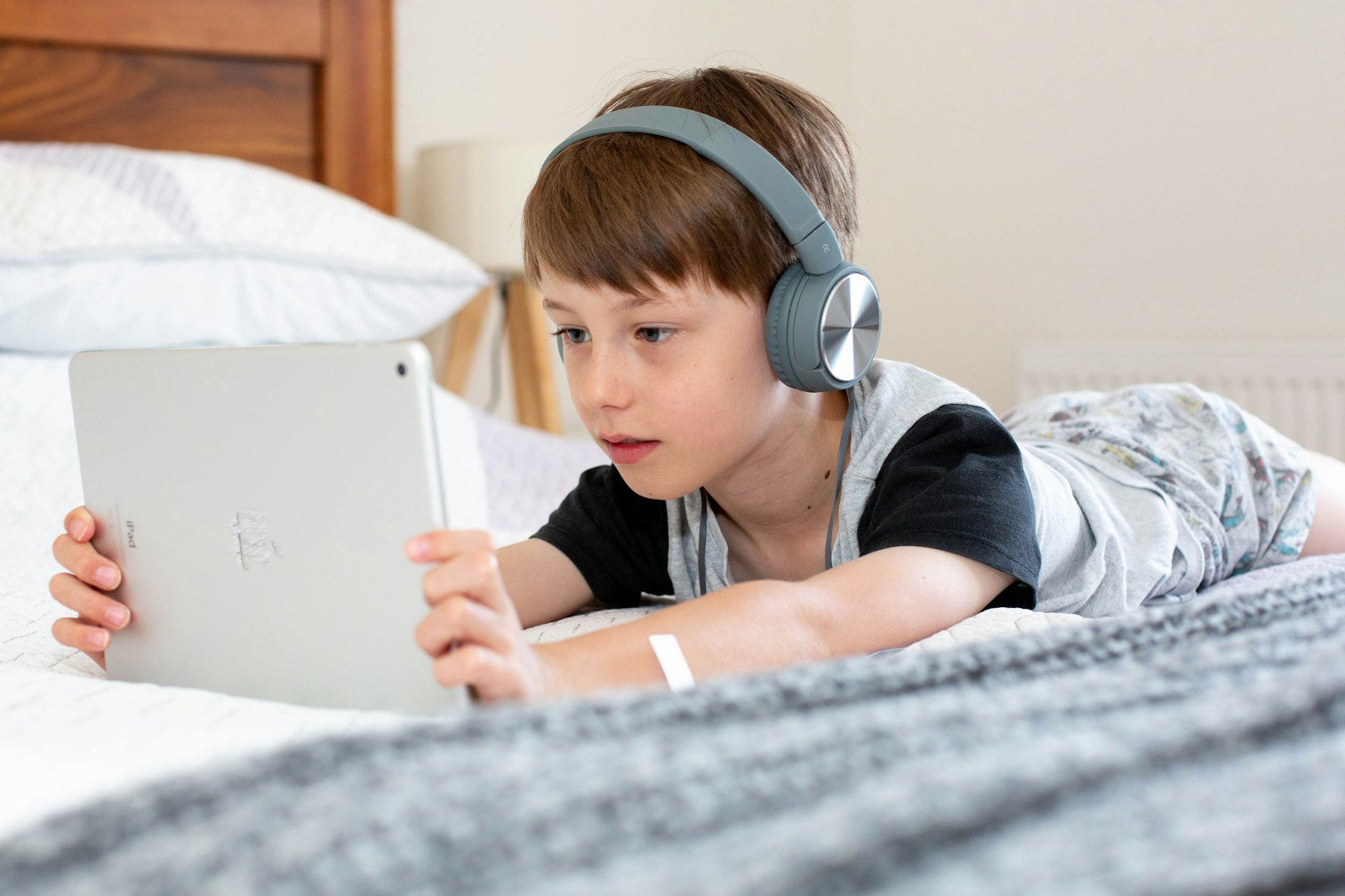 Photo by Emily Wade boy in blue shirt wearing headphones lying on bed