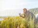 man reading book on beach near lake during daytime
