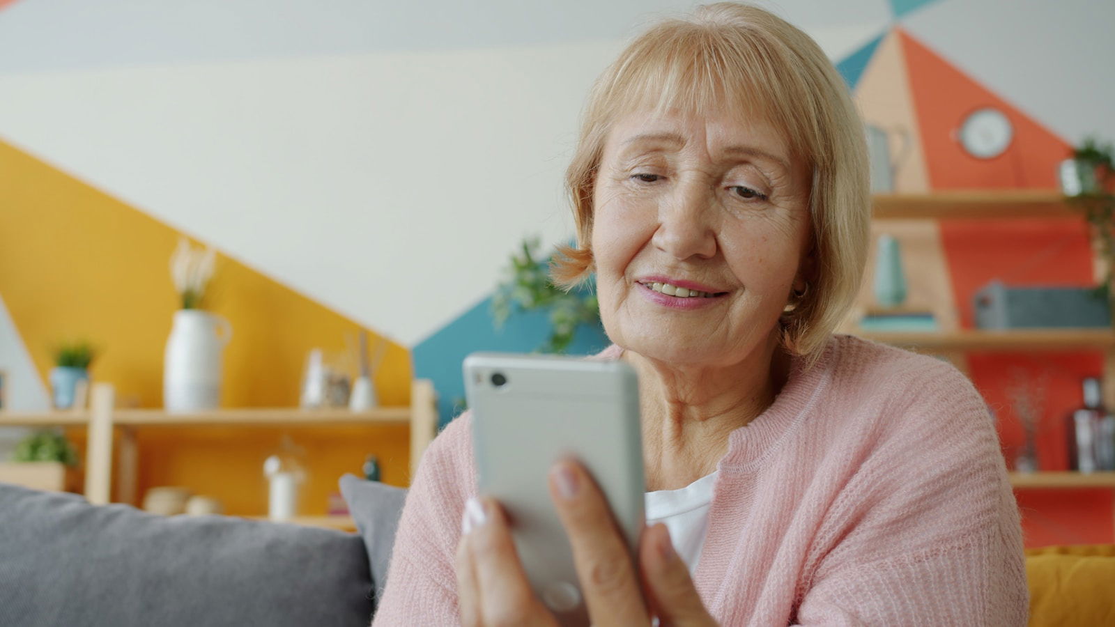 Photo by Vitaly Gariev Elderly woman smiling while looking at smartphone.