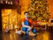 a boy sitting on the floor in front of a christmas tree