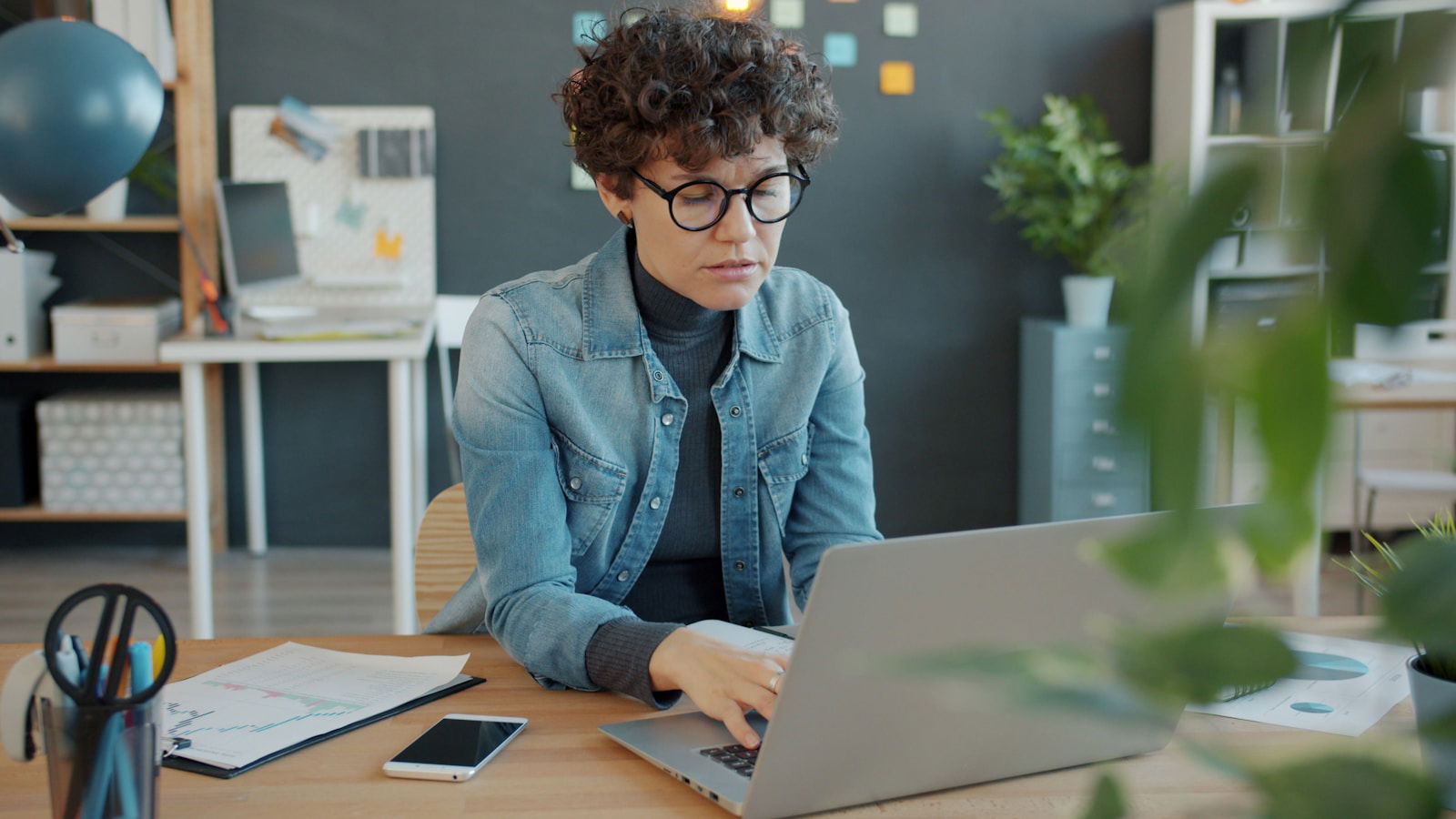 Woman with curly hair working on laptop at desk.
