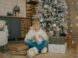 a young boy sitting on the floor next to a christmas tree