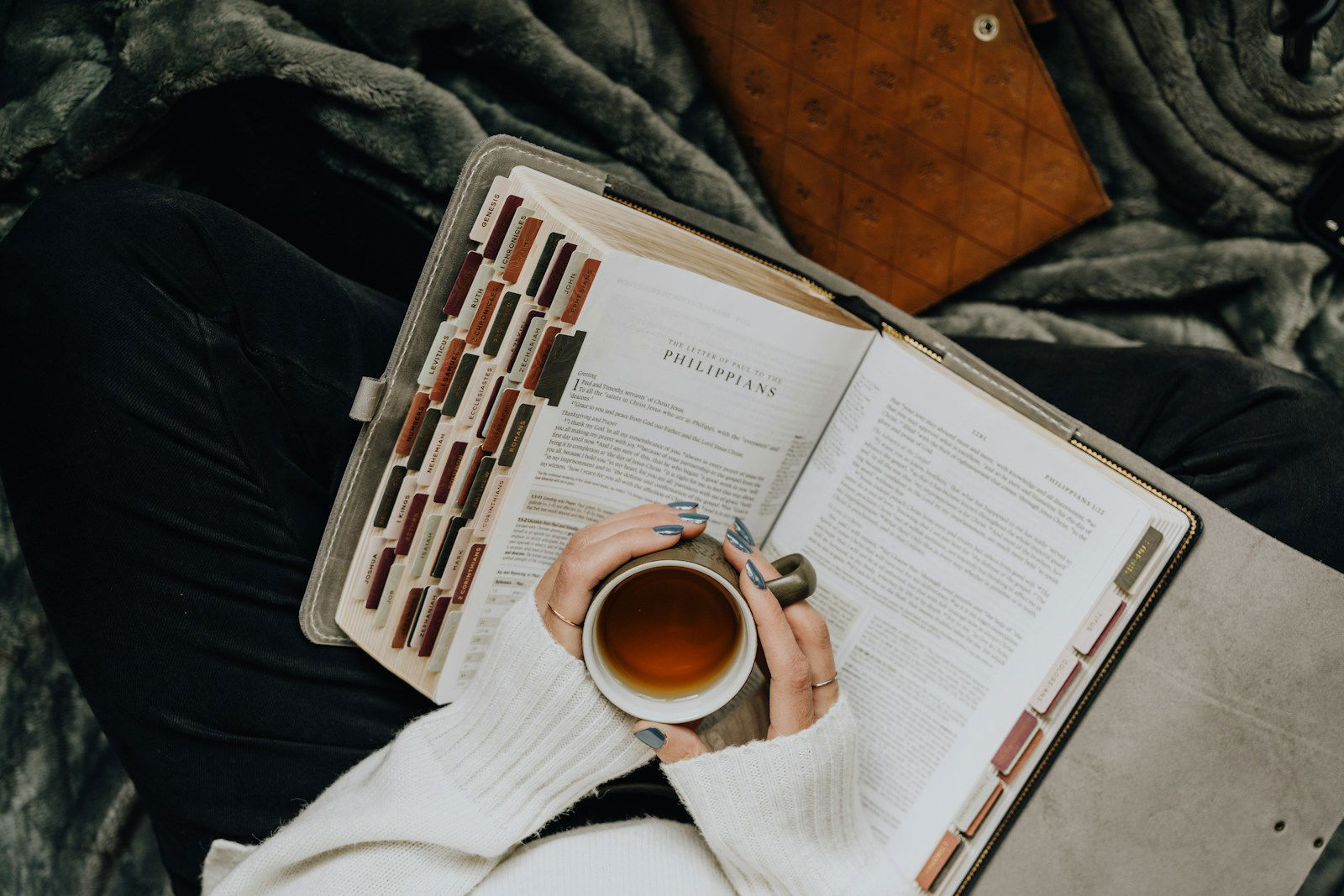 A person is holding a cup of tea and reading a book