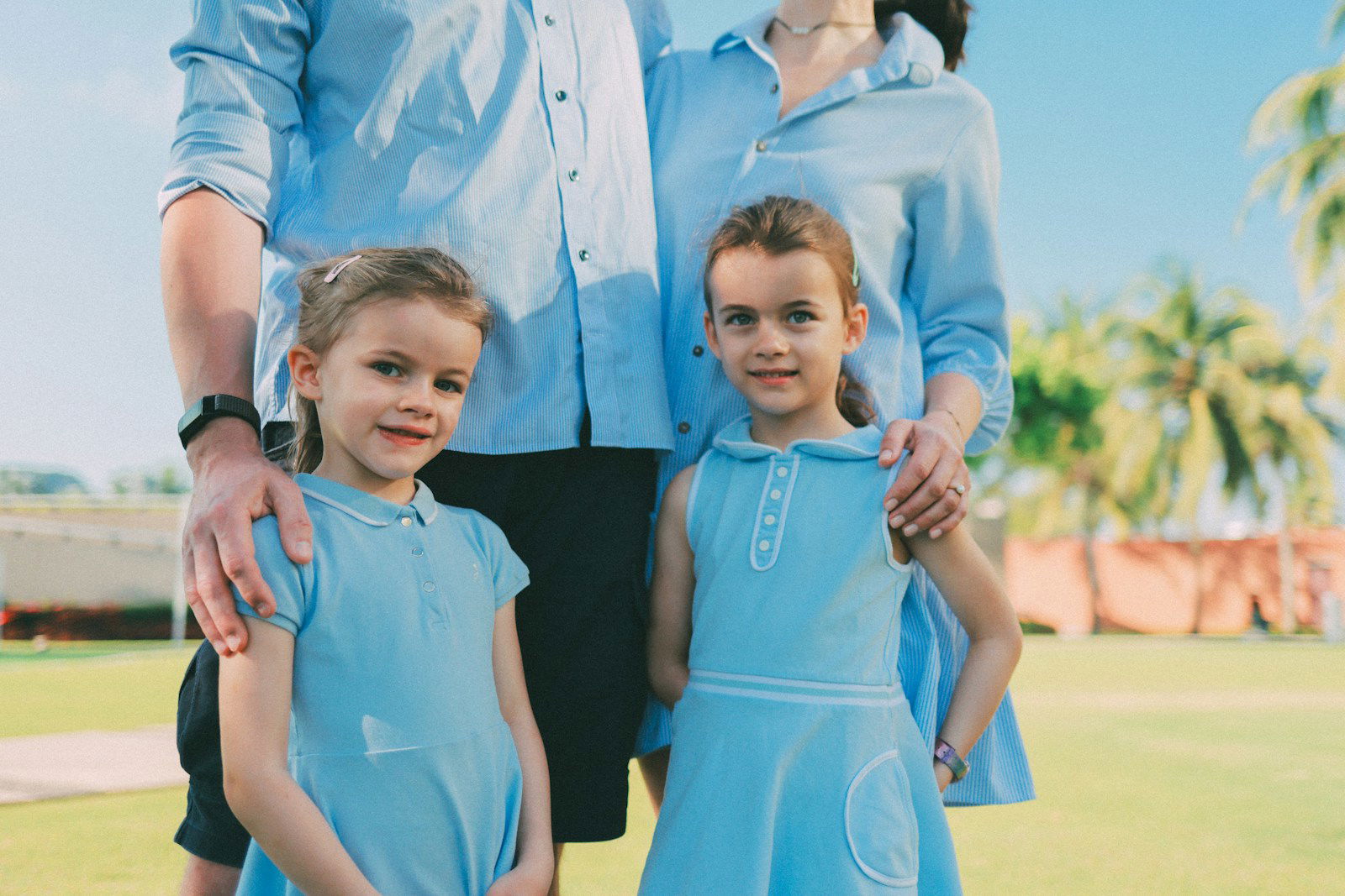 Two young girls stand with parents outdoors.