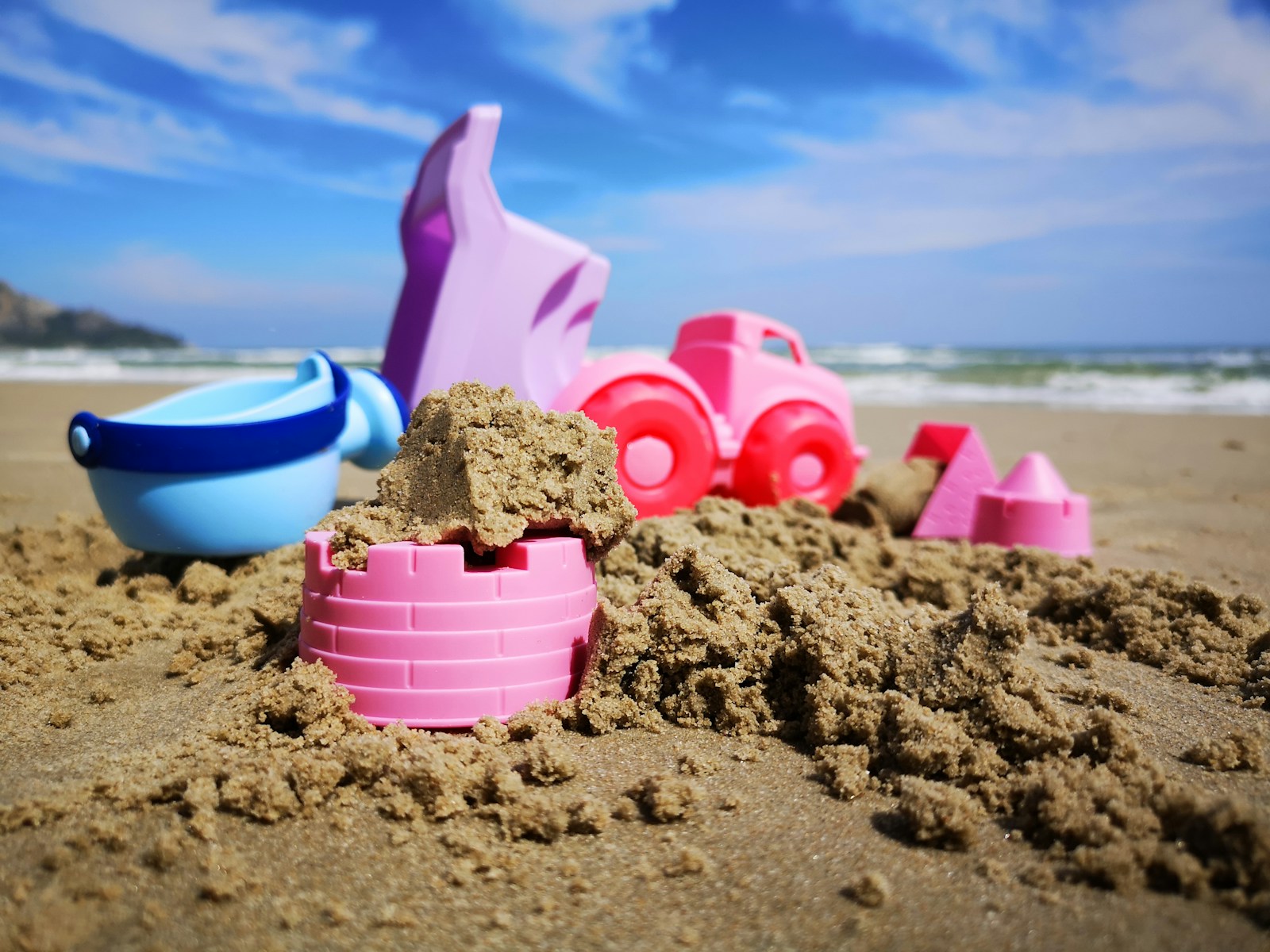 a pink sand castle with a pink toy car and a blue toy boat