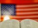An open book with a blurred american flag background.