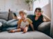 a woman and a child sitting on a couch looking at a cell phone