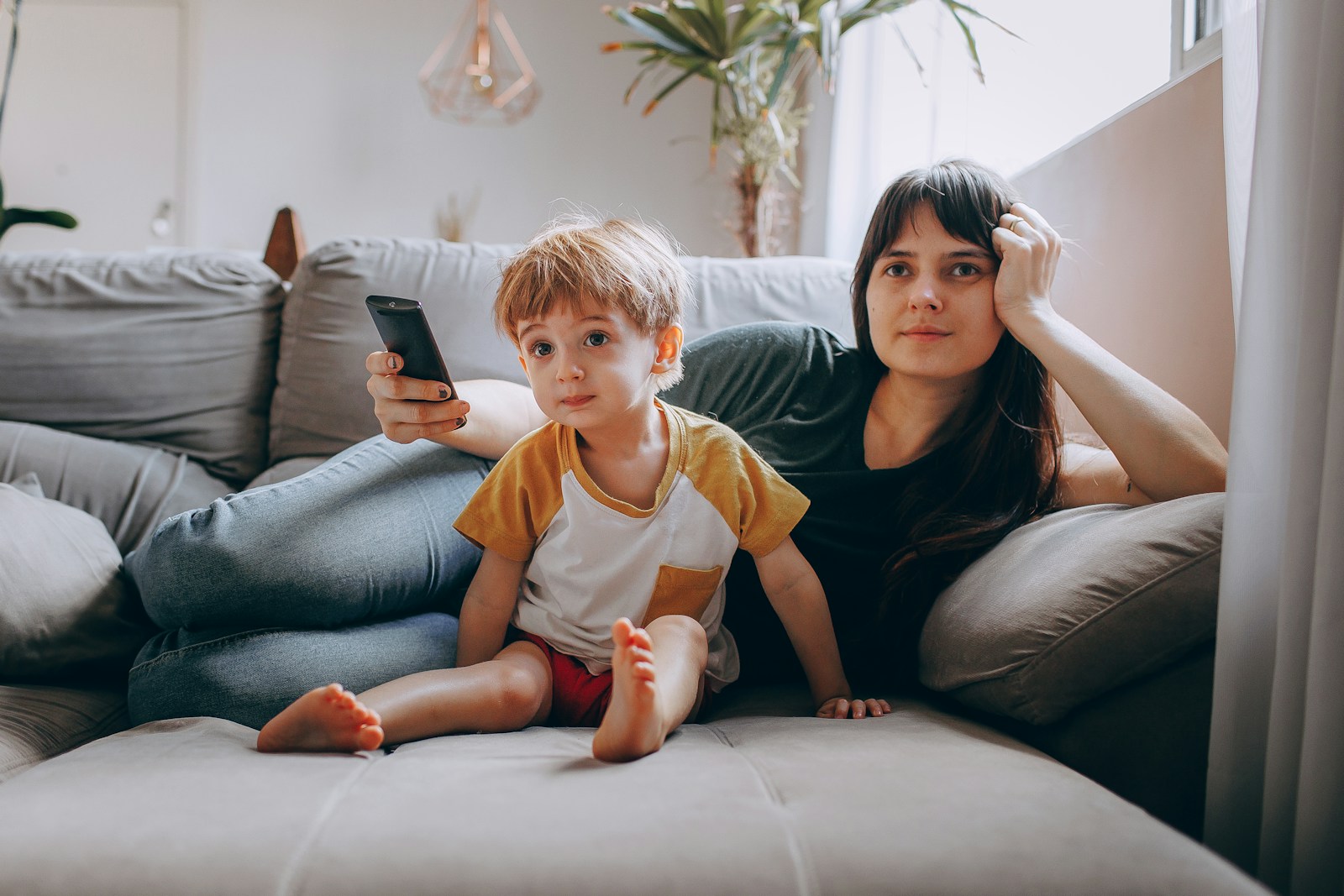 Photo by Helena Lopes a woman and a child sitting on a couch looking at a cell phone